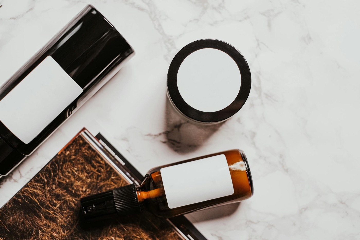Cosmetic bottles and an open glass bottle of ethanol-based formula on a marble surface