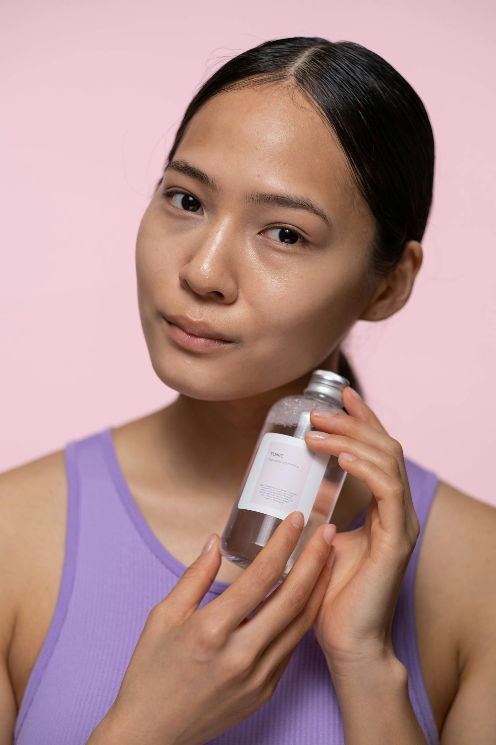 Woman holding a snail mucin essence bottle against a soft pastel background, the K-beauty format that popularised the ingredient